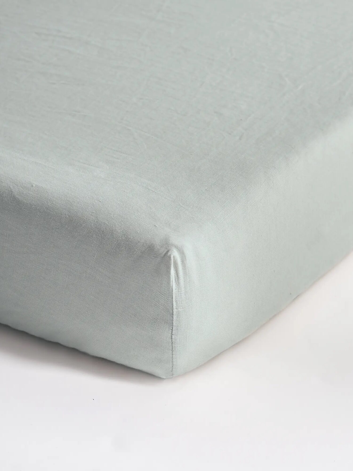 Close-up of a light gray fitted sheet corner on a mattress, showcasing its smooth texture and snug fit.