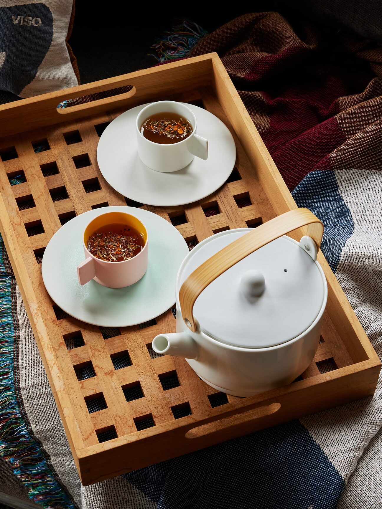 A wooden tray with a teapot and two cups of tea on saucers. The tray is on a blanket-covered surface.