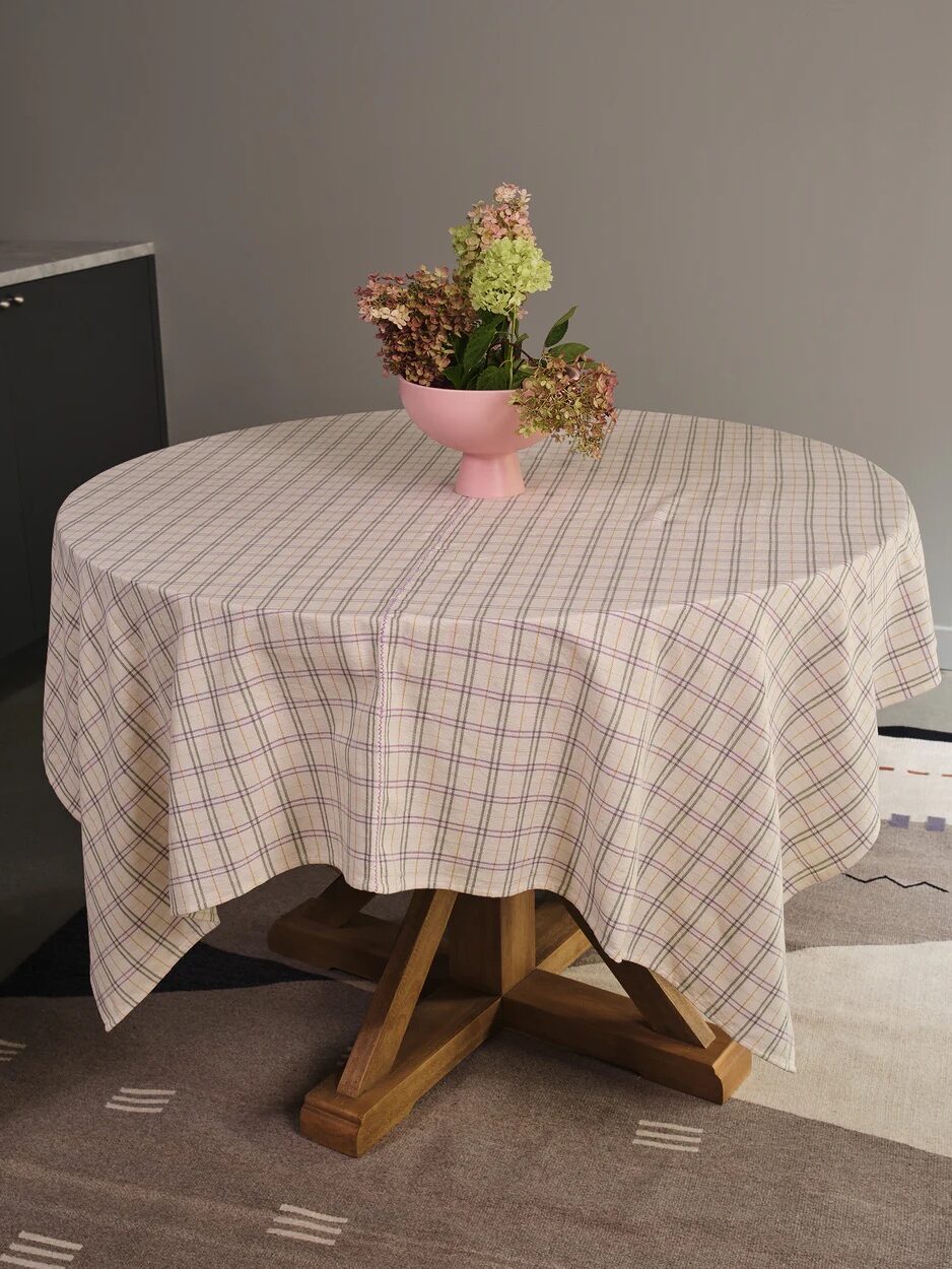 A round table with a plaid tablecloth and a pink vase holding flowers in the center.