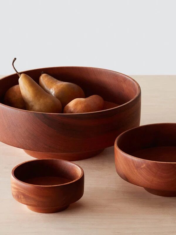 Three nested wooden bowls on a light wooden surface, with the largest bowl containing several pears.