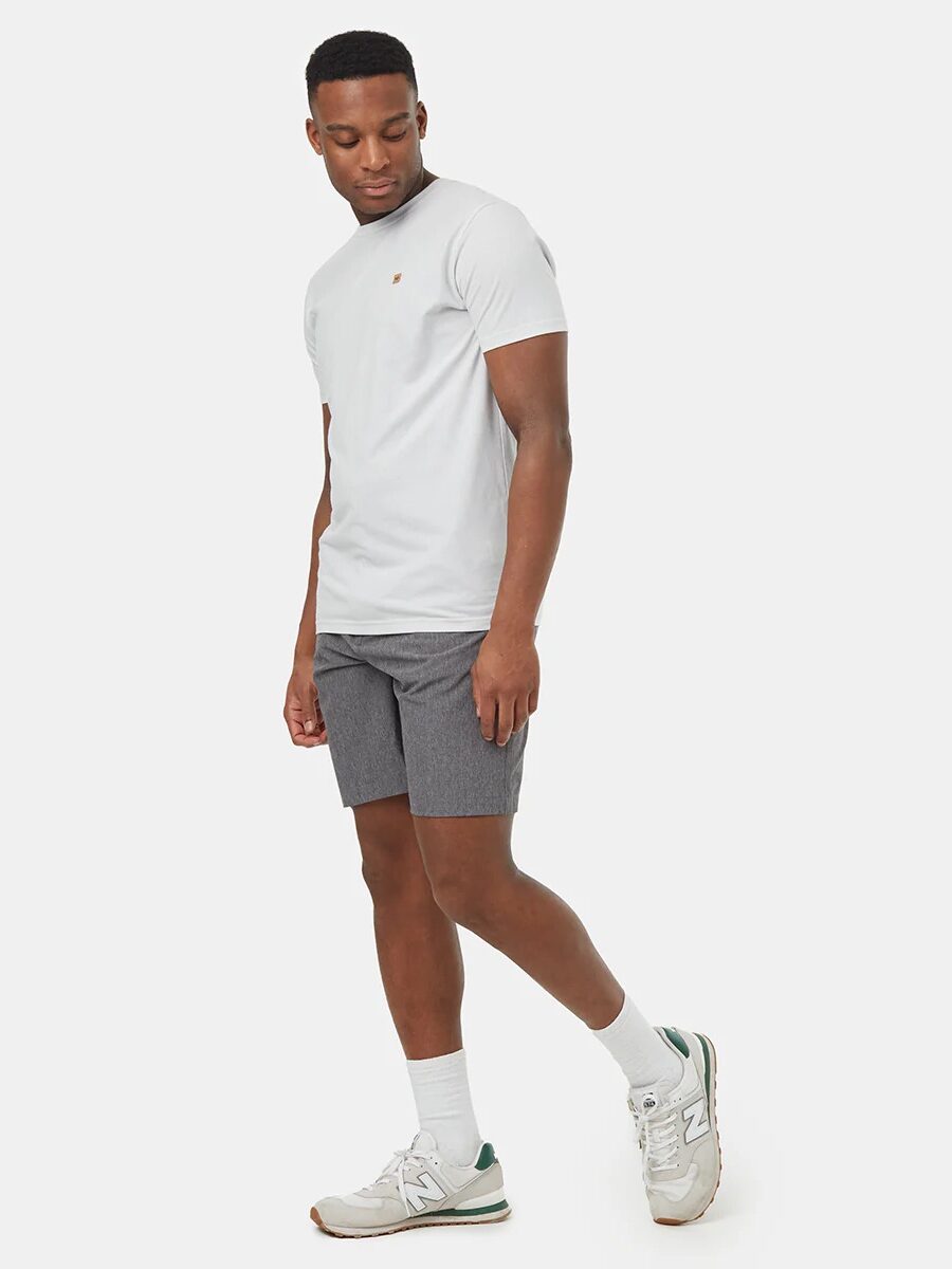 A person wearing a white t-shirt, gray shorts, white socks, and sneakers stands against a plain background.