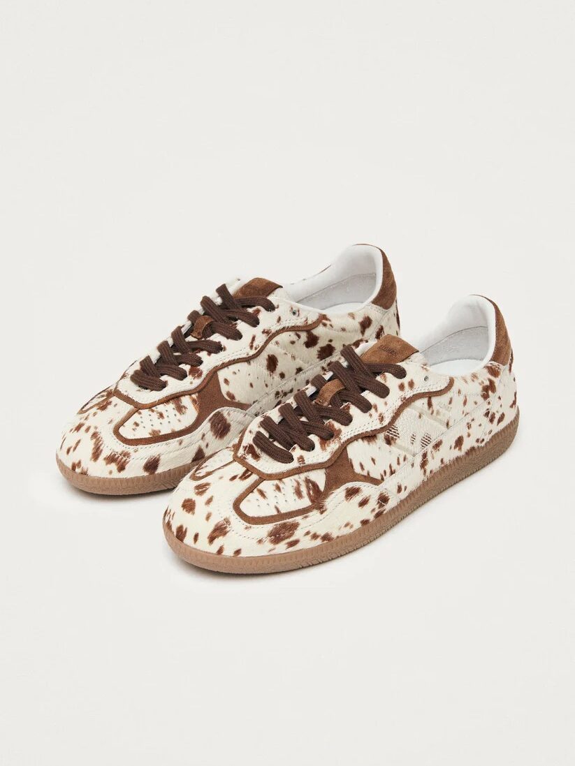 Pair of sneakers with a brown and white cow print design and brown laces on a white background.