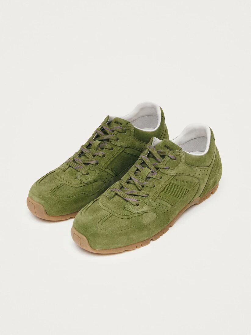 A pair of olive green sneakers with brown gum soles and matching laces on a plain white background.