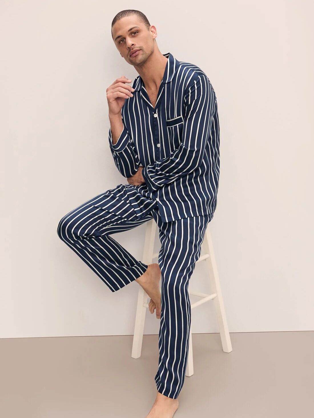 A person in blue and white striped pajamas sits on a white stool against a light background.