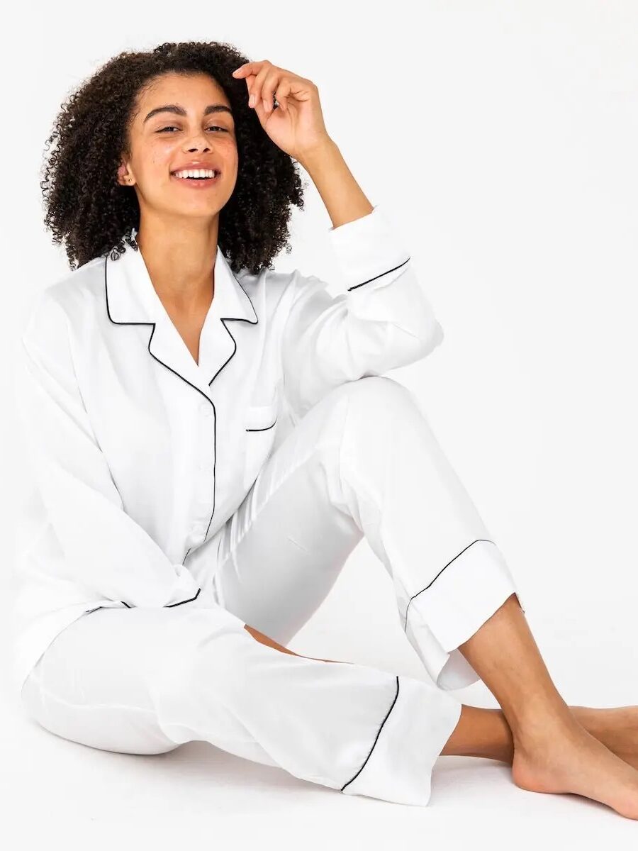 Person in white pajamas with black trim, sitting on the floor, smiling against a plain background.