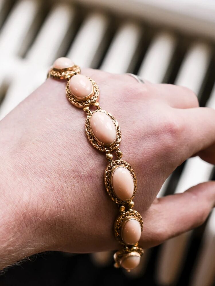 A hand wearing a gold bracelet with oval pink stones.