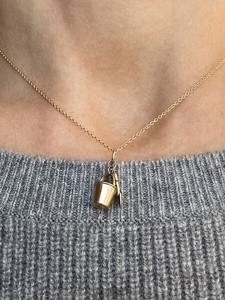 Gold necklace with a small bucket pendant worn over a gray knitted sweater.