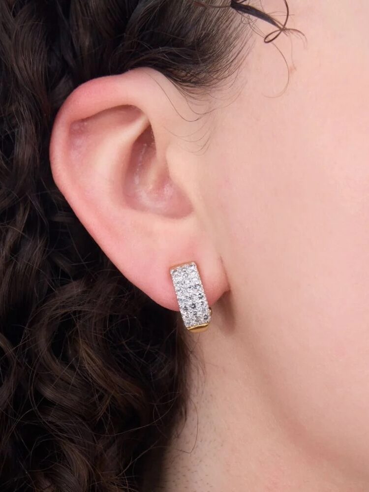 Close-up of a person wearing a rectangular, silver-and-gold earring with embedded sparkling gems.