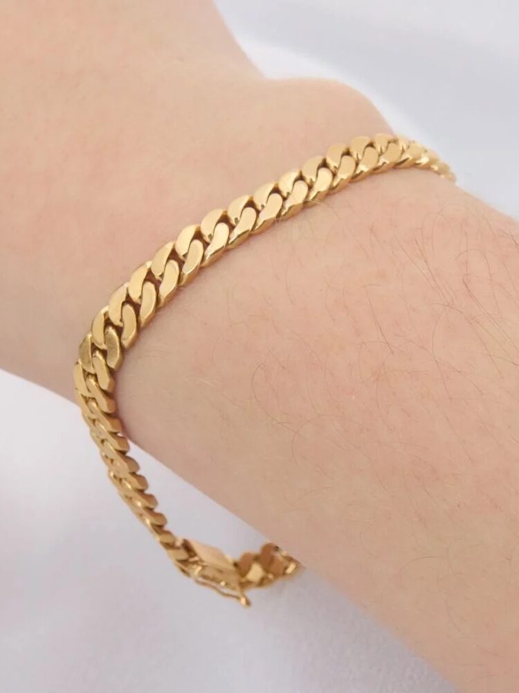 A gold chain bracelet on a person's wrist against a white background.