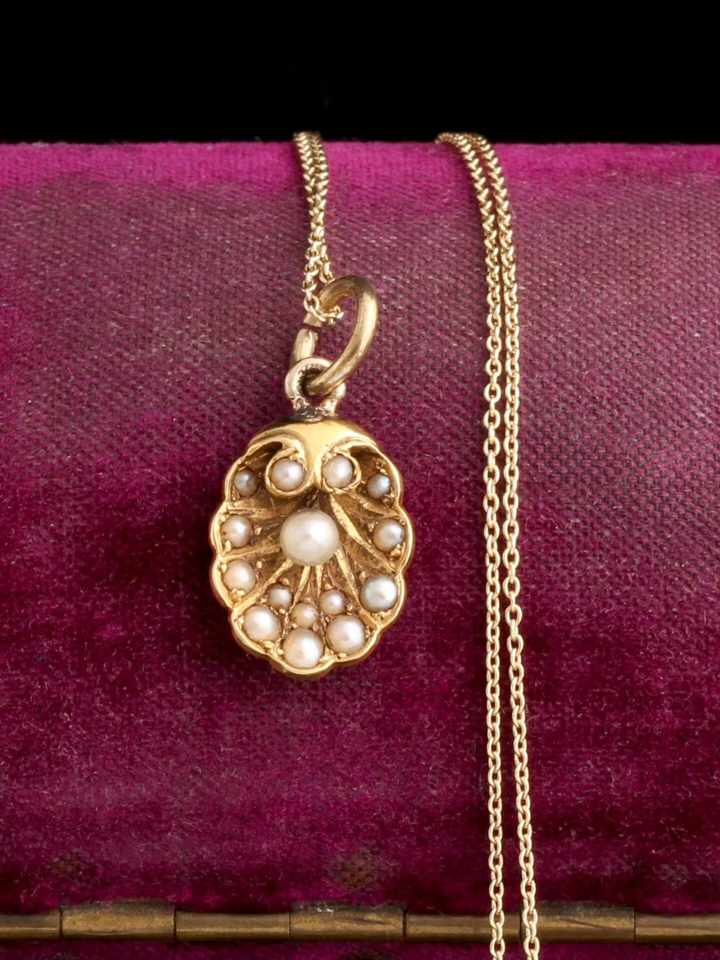 A gold pendant necklace with pearls is displayed on a purple velvet surface.