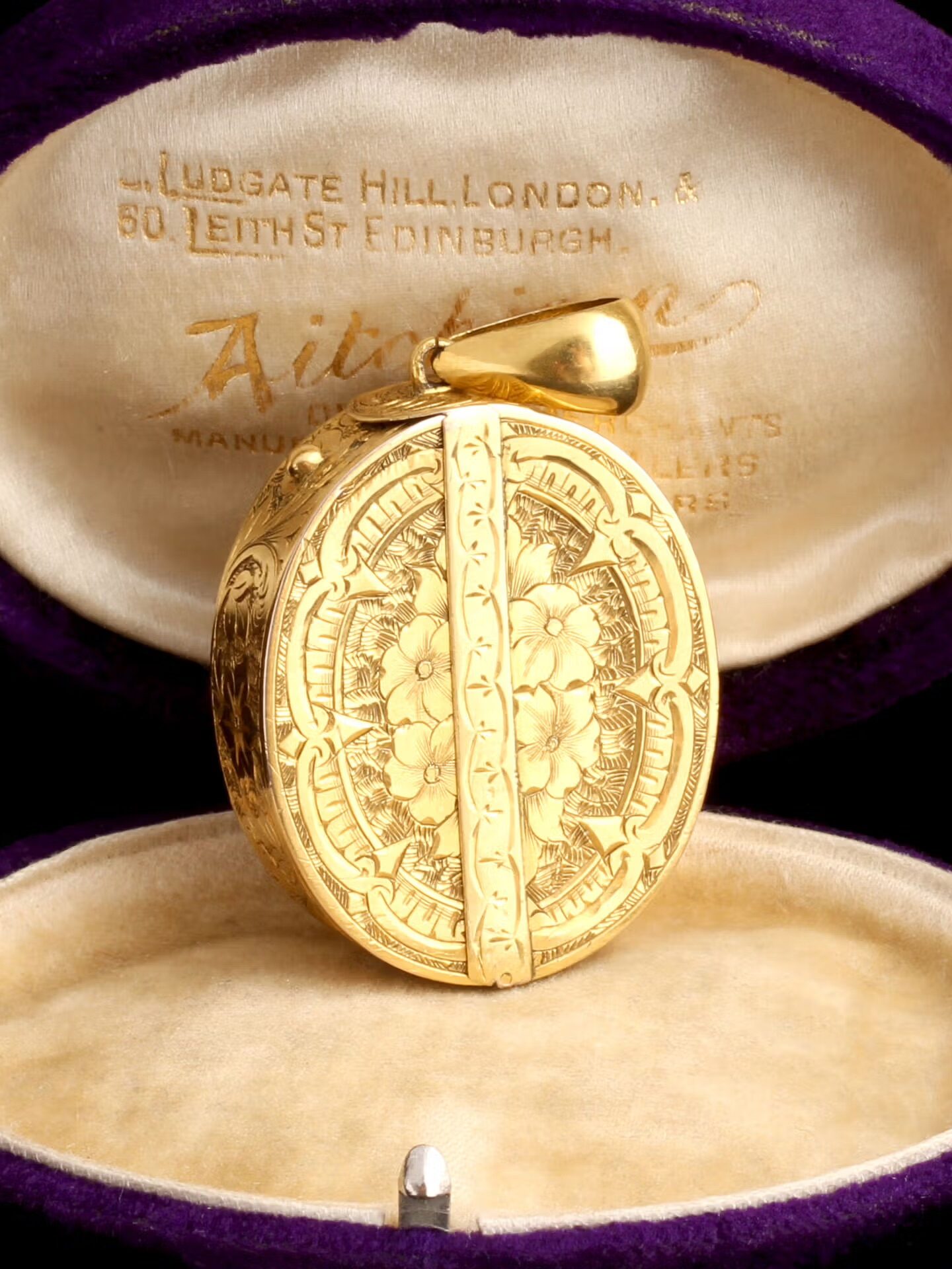 Gold locket with intricate floral design inside a purple and cream velvet box with inscriptions on the inner lid.