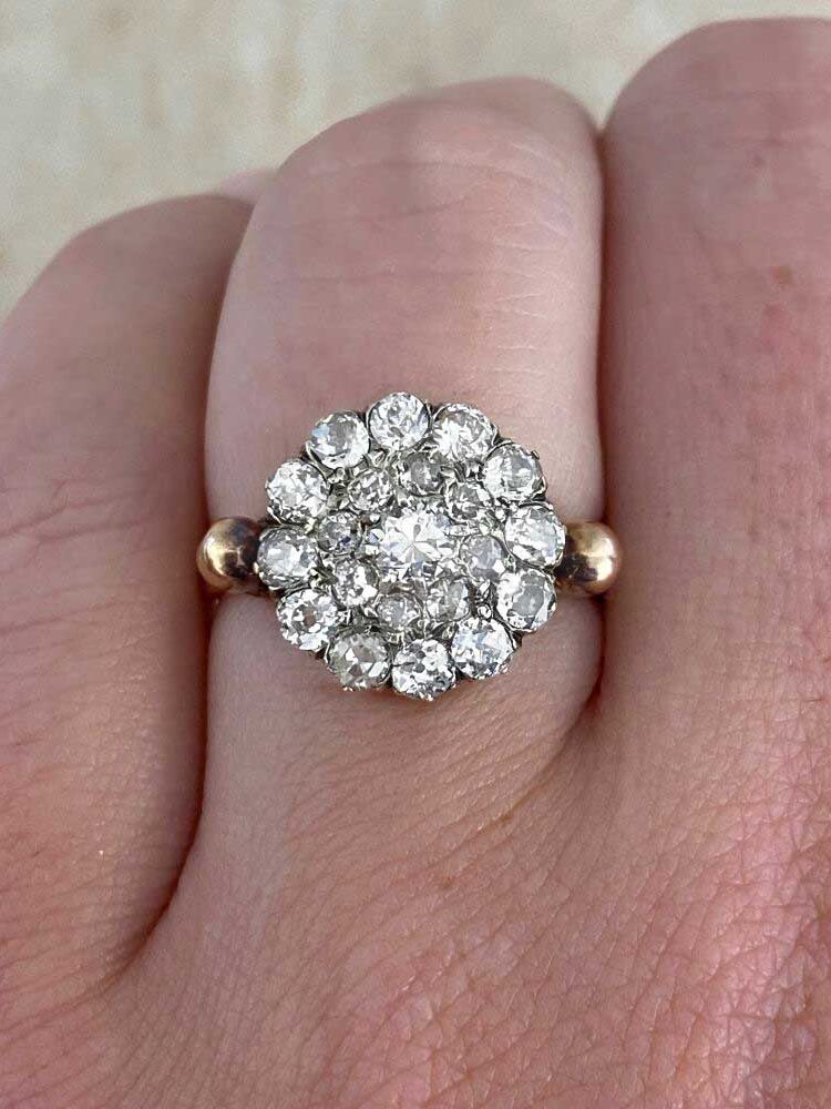 Close-up of a gold ring on a finger, featuring a large, circular cluster of small sparkling diamonds.