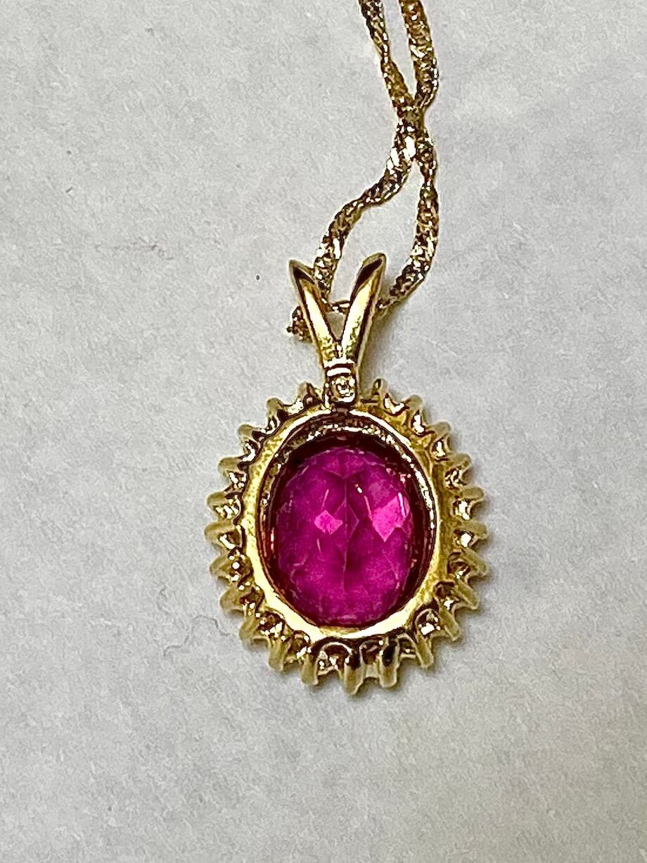 Gold necklace with a circular pendant featuring a pink gemstone set in a sunburst design.