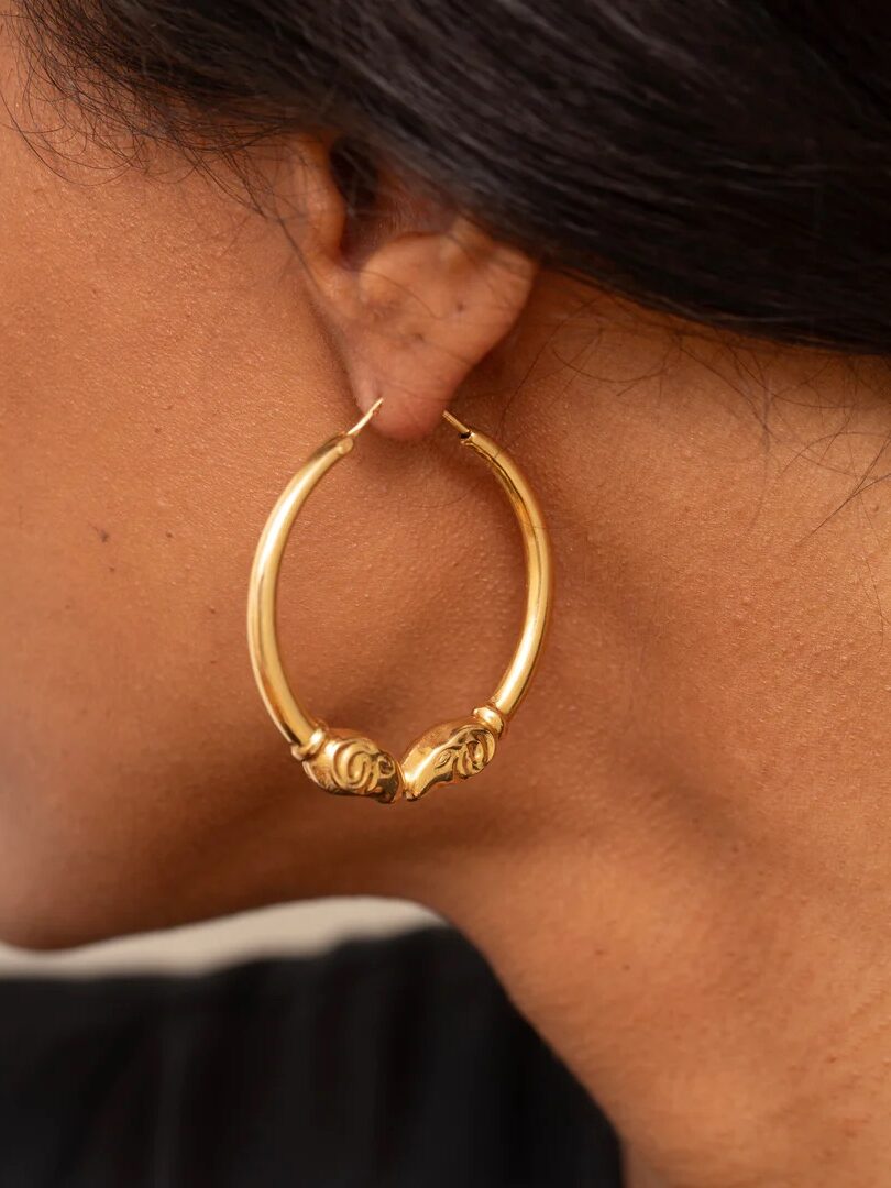 Close-up of a person wearing a large gold hoop earring with a decorative element near the earlobe.