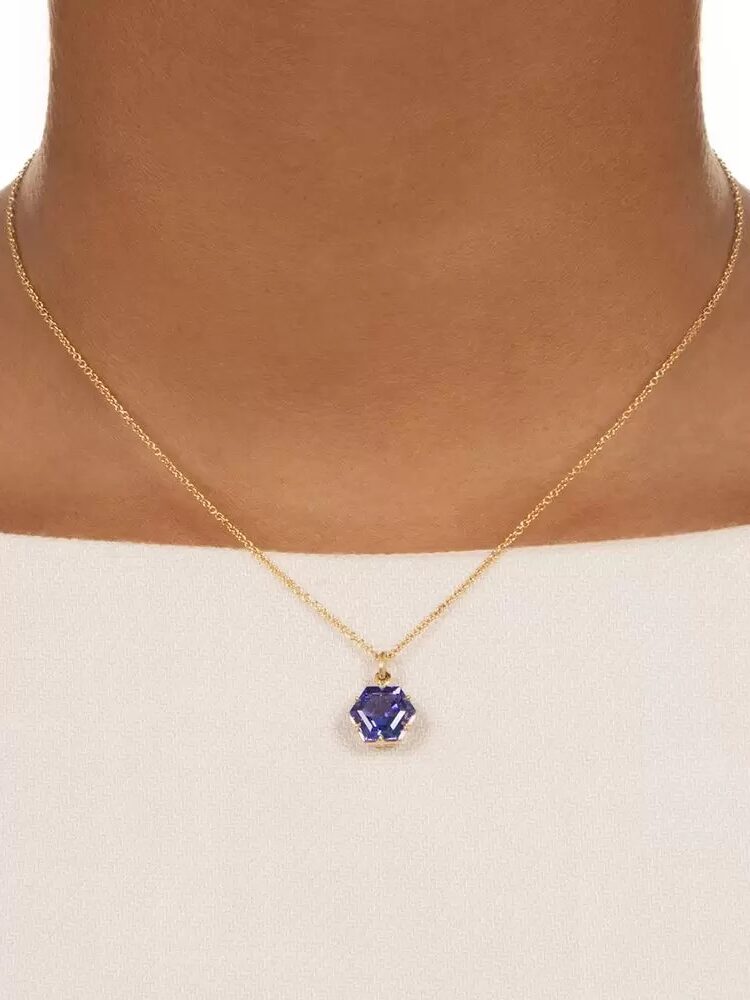 A gold necklace featuring a hexagonal blue gemstone pendant worn around a person's neck.