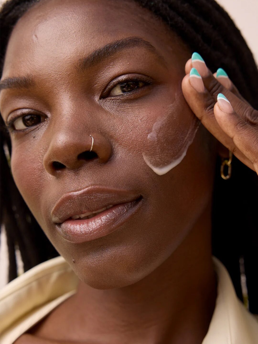 A person applies cream to their cheek with a focused expression, showcasing a skincare routine.