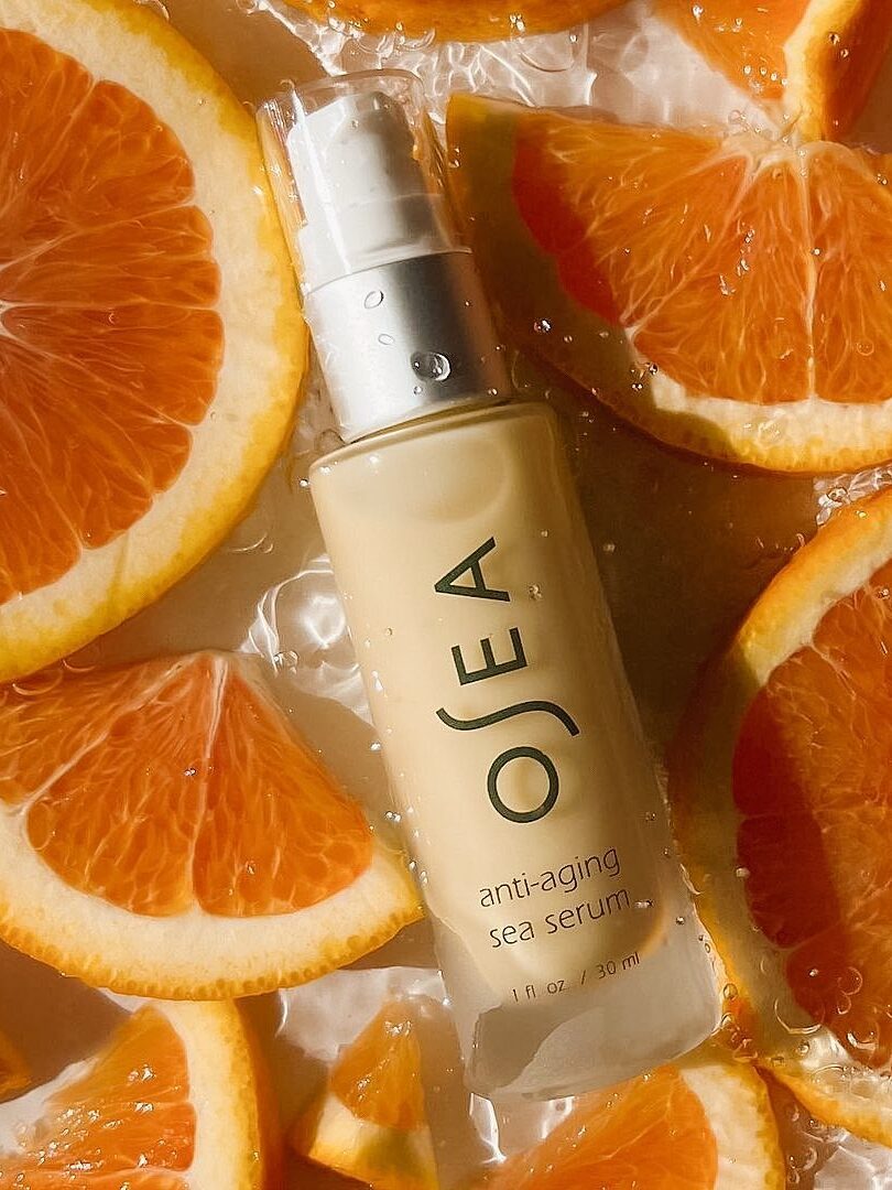 A bottle of Osea anti-aging sea serum surrounded by sliced oranges.