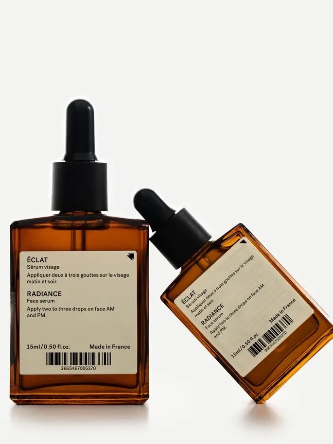 Two amber dropper bottles labeled "ÉCLAT Radiance Face Serum" positioned upright and tilted, against a neutral background.