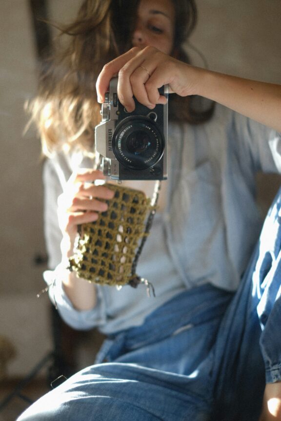 Person in denim holding a camera, wearing a beige shirt, taking a photo with sunlight illuminating the scene.