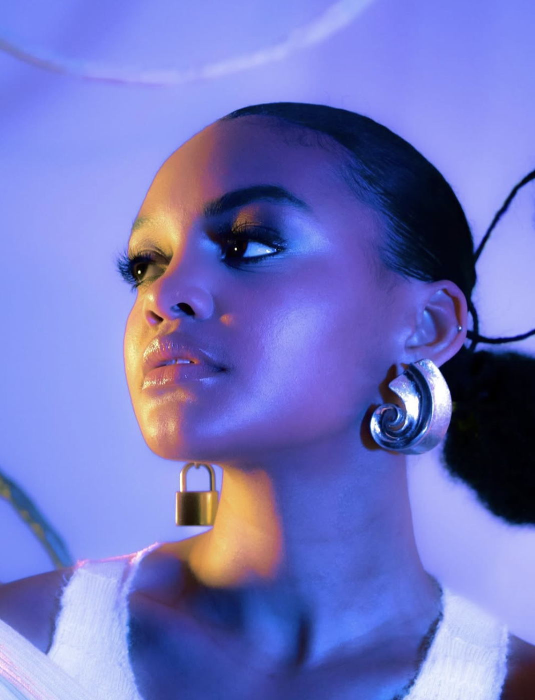 A person with large earrings looks to the side, illuminated by blue and purple lighting.