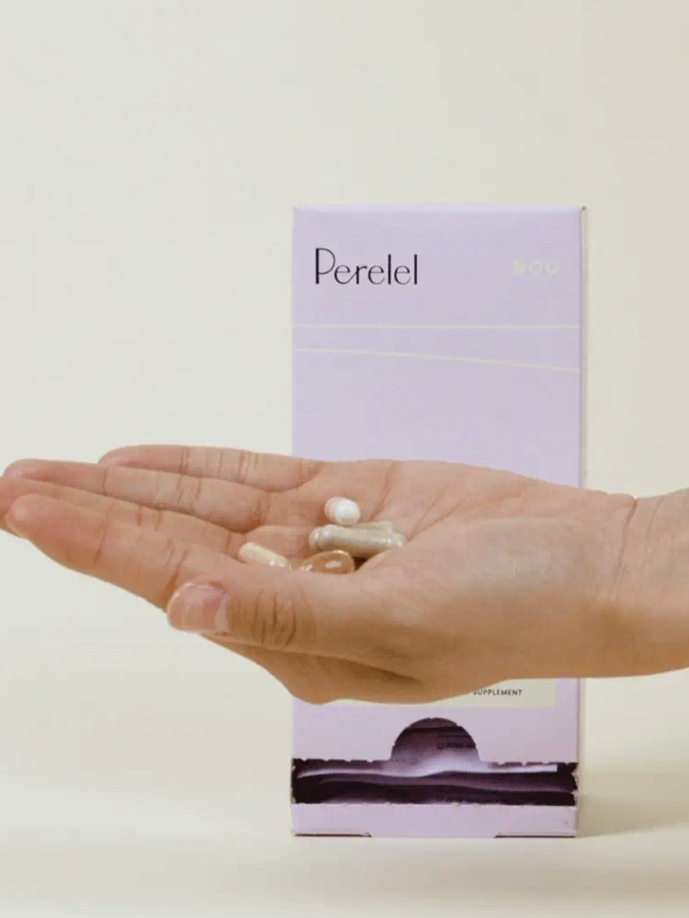 A hand holds several pills in front of a box labeled "Perelel" against a light background.