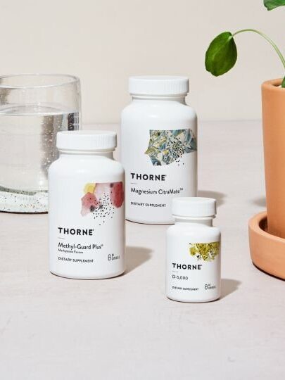 Three bottles of Thorne supplements on a table next to a glass of water and a potted plant.