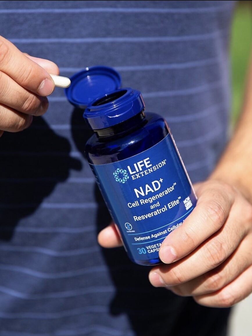 Person holding an open bottle of Life Extension NAD+ Cell Regenerator and Resveratrol Elite capsules, with one capsule in hand.