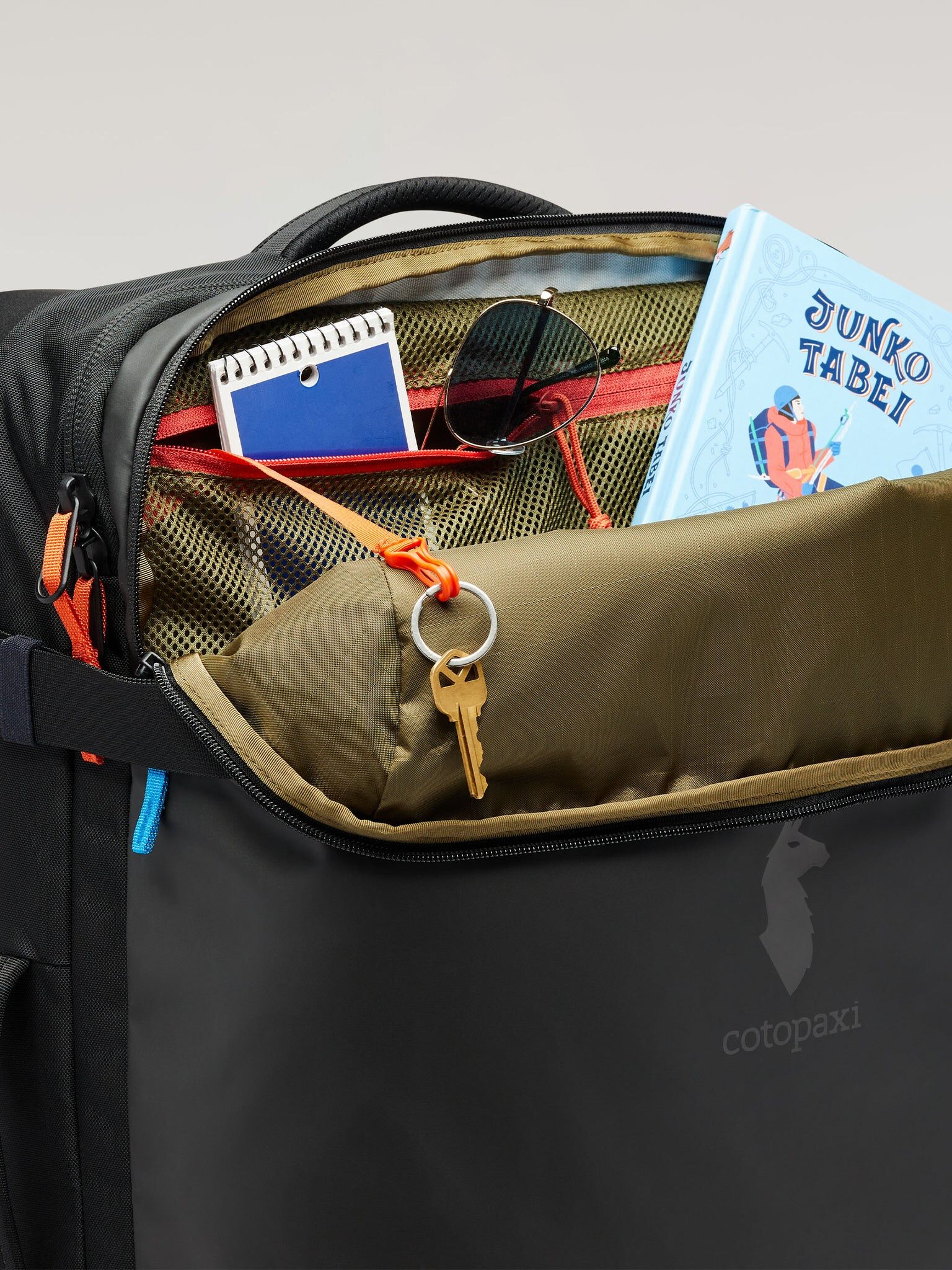 Open backpack with a book, sunglasses, notebook, and a key in the front pocket.