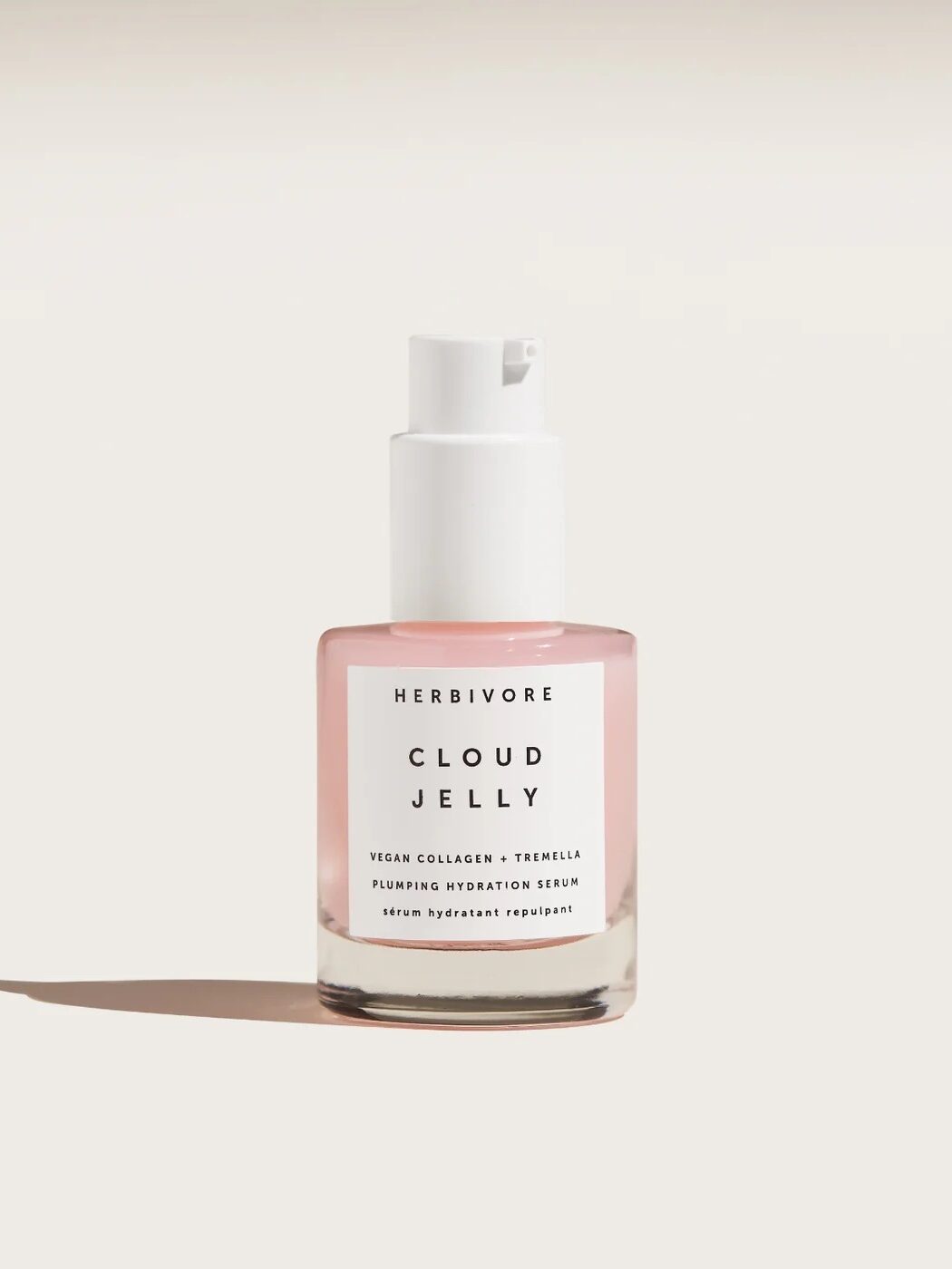 A clear bottle with a pink liquid, labeled "Herbivore Cloud Jelly," featuring a white pump top, standing on a solid surface casting a shadow.