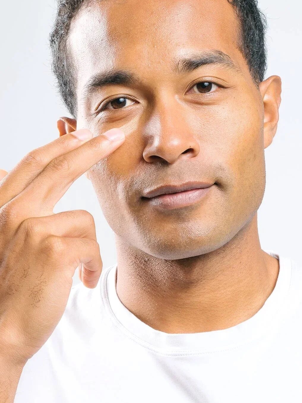 Person in a white shirt touches their face with two fingers against a plain background.