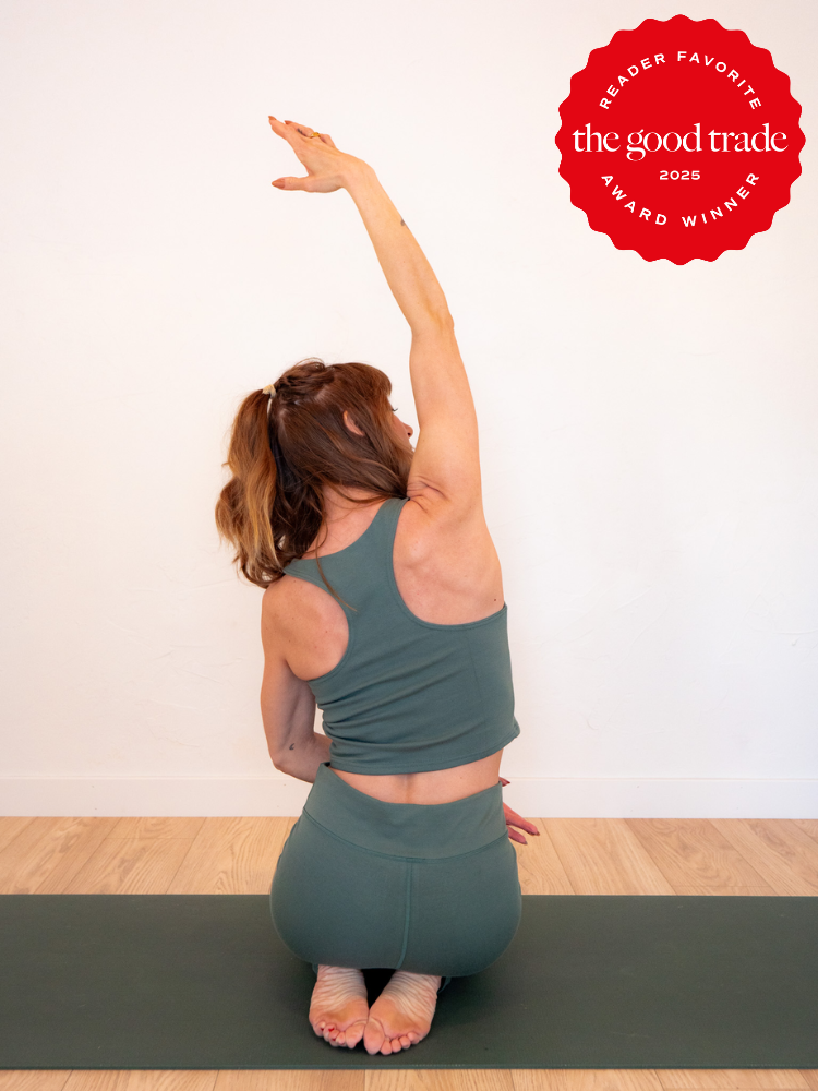 A person in a green yoga outfit performs a seated side stretch on a mat. A red badge on the image reads "Reader Favorite, the good trade, 2023 Award Winner.