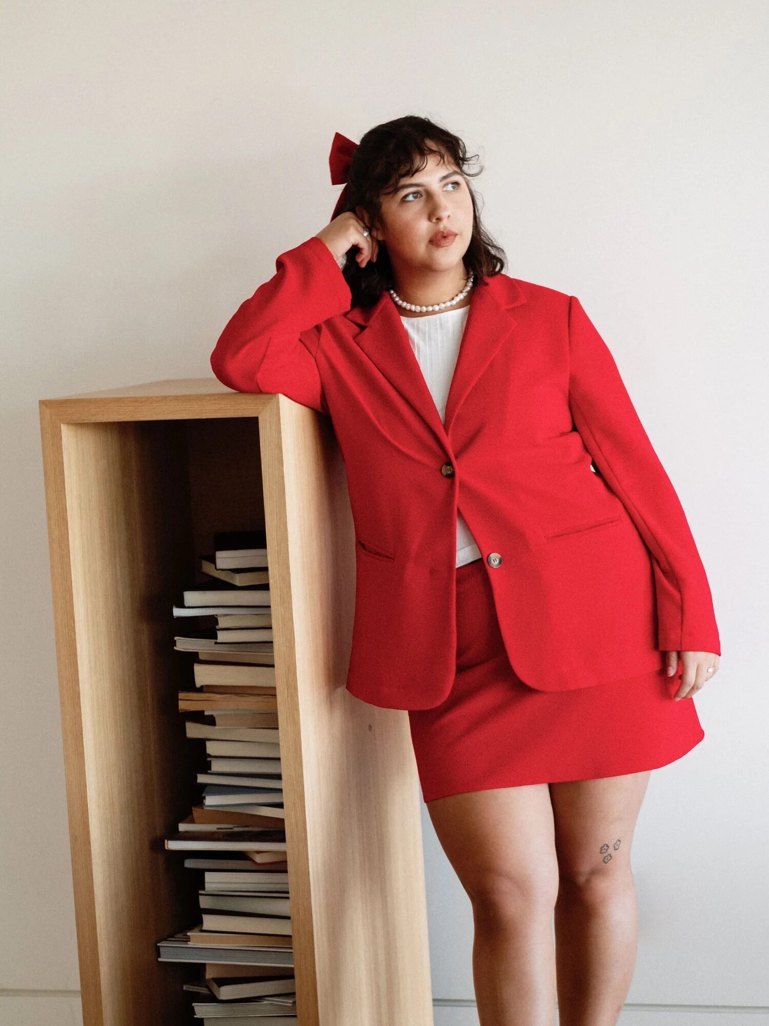 Person in a red suit leans against a wooden shelf filled with books.