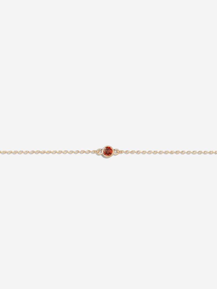 A delicate gold chain bracelet featuring a small round orange stone set in the center.