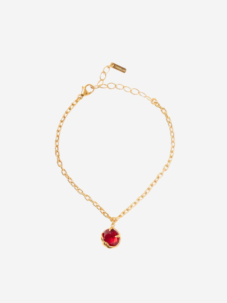 Gold bracelet with a chain link design and a red gemstone charm.