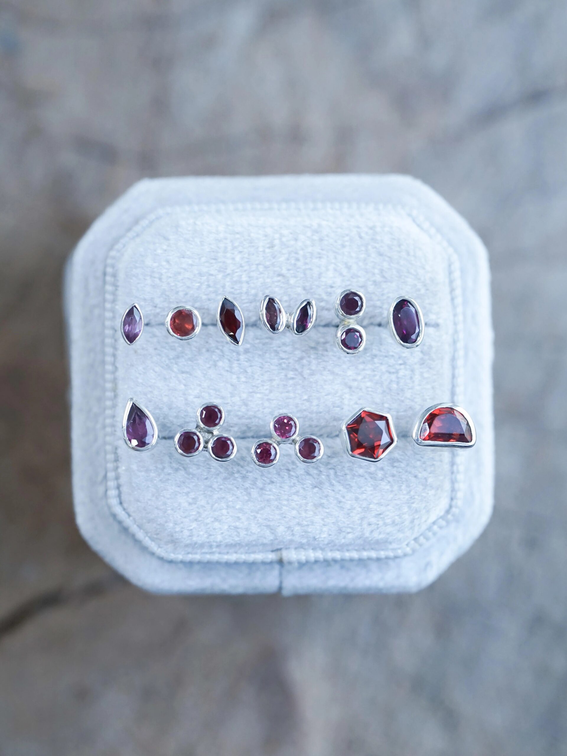 A display of various red gemstone earrings on a gray cushioned surface.