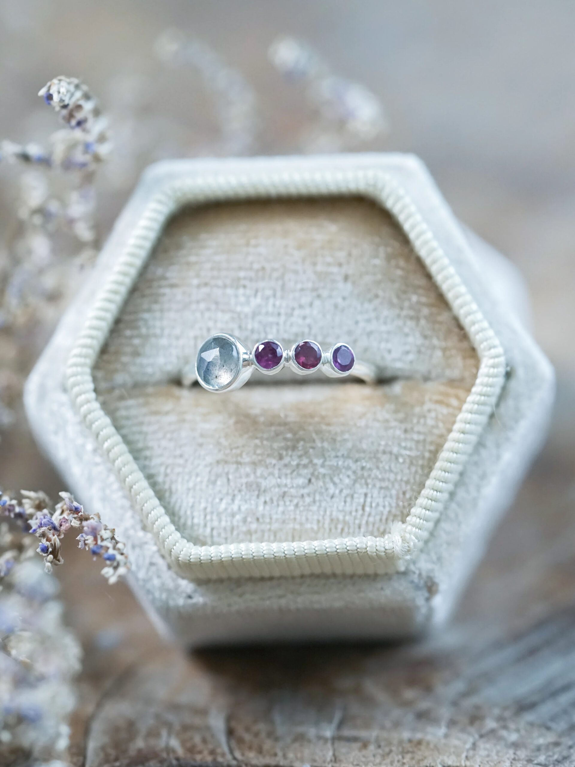 A silver ring with a row of five gemstones in varying sizes on a hexagonal velvet box.