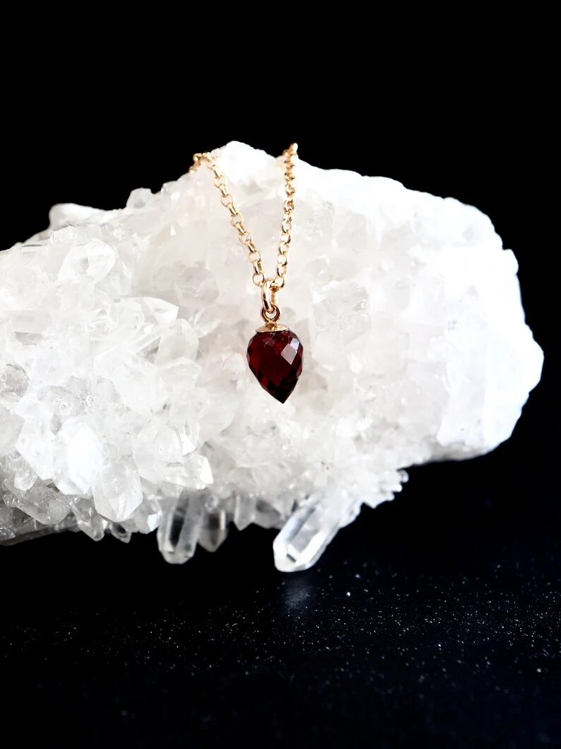 A gold chain with a red teardrop pendant displayed on a large white crystal against a black background.