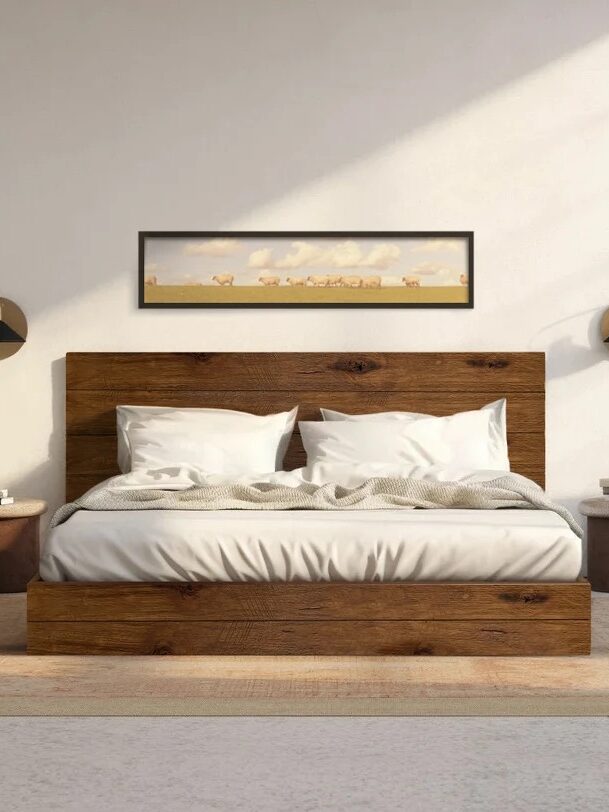 A minimalist bedroom with a wooden bed, white bedding, two round side tables, wall sconces, a small plant, and landscape artwork above the headboard. Natural light fills the room.