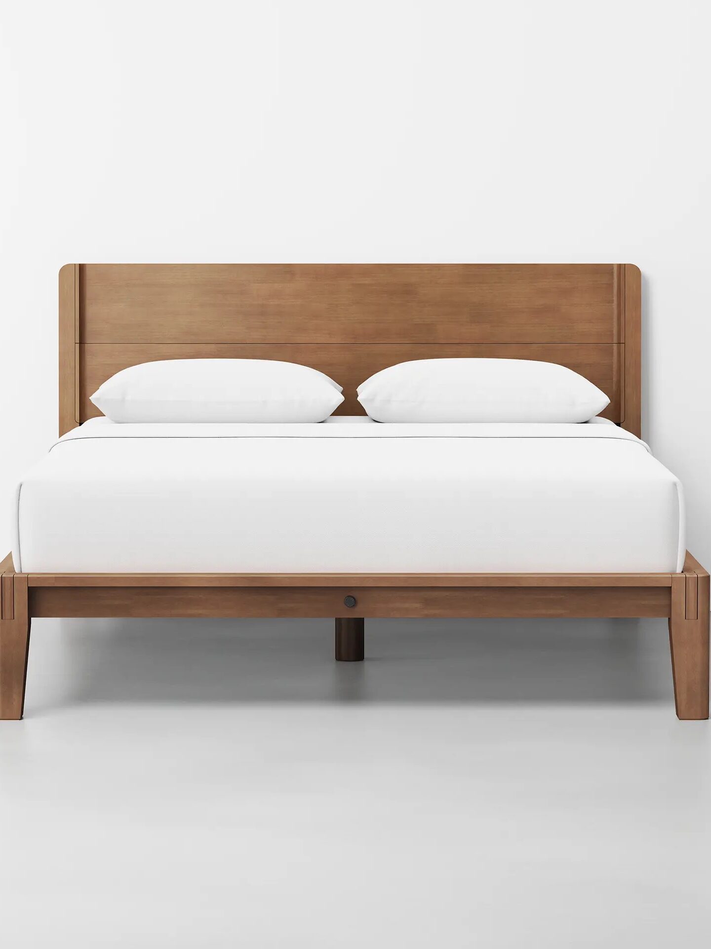 Wooden bed frame with a simple design, featuring a white mattress and two pillows on a light gray floor.