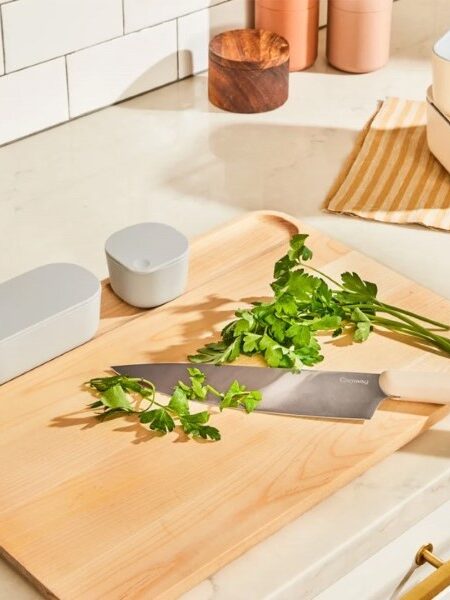 Knife and fresh parsley on a wooden cutting board, with food storage containers nearby on a kitchen countertop.