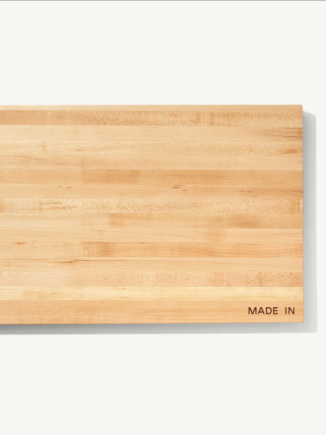 Rectangular wooden cutting board with light and dark grain patterns, featuring the text "Made In" in the bottom right corner.