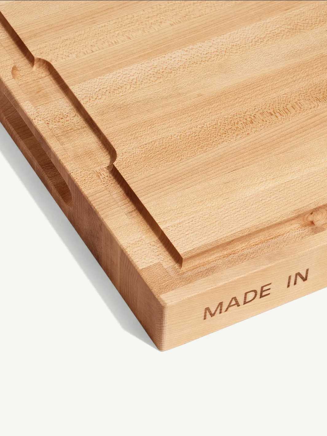 A wooden cutting board with grooves, featuring the engraved text "MADE IN" on one side.