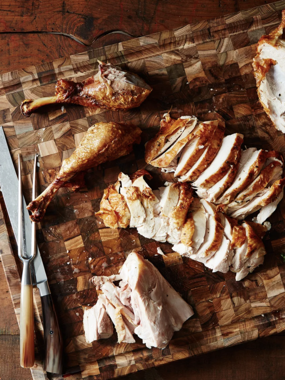 Sliced roasted turkey on a wooden cutting board with a carving knife and fork on the side.