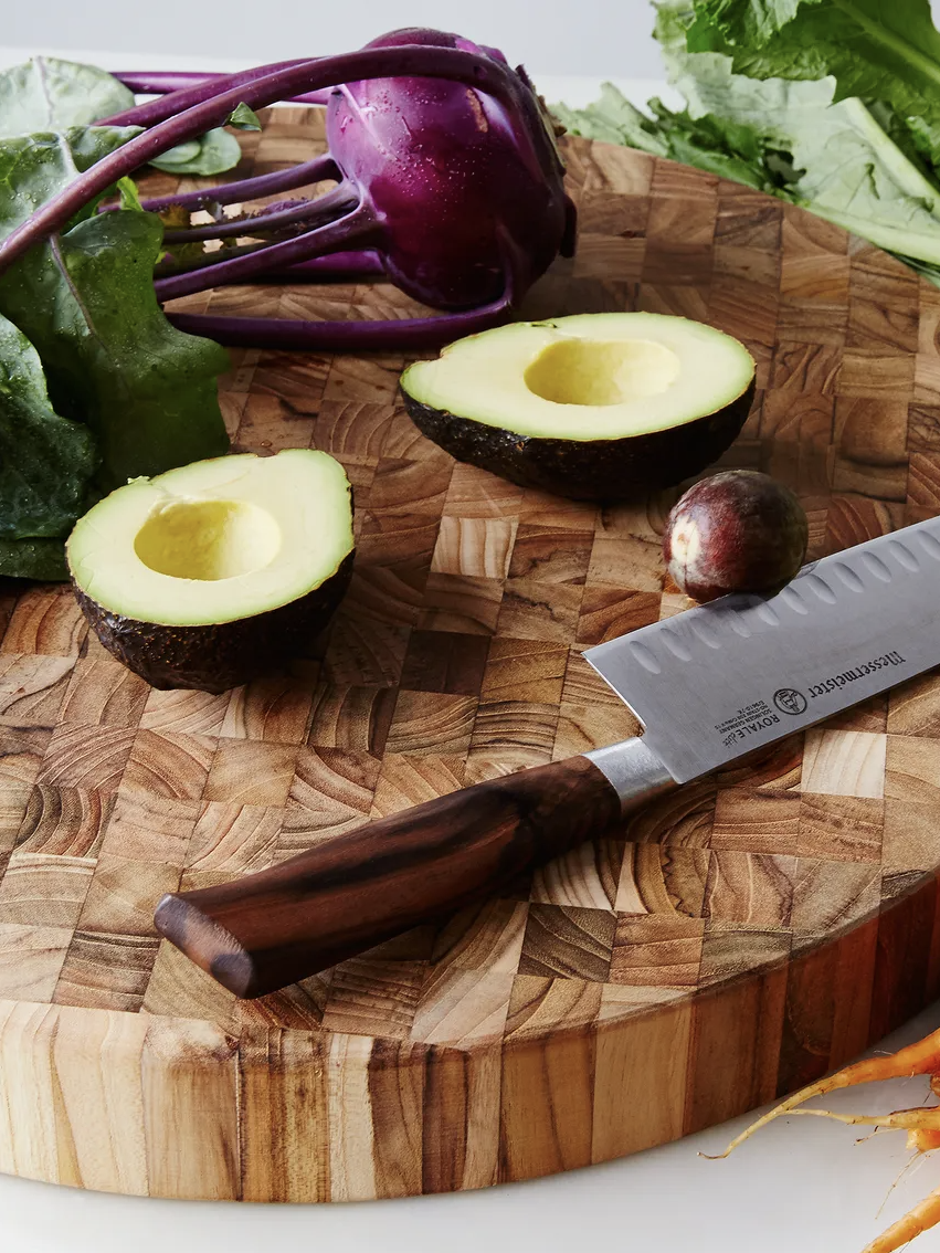 Knife on a wooden cutting board with halved avocado, kohlrabi, and leafy greens.