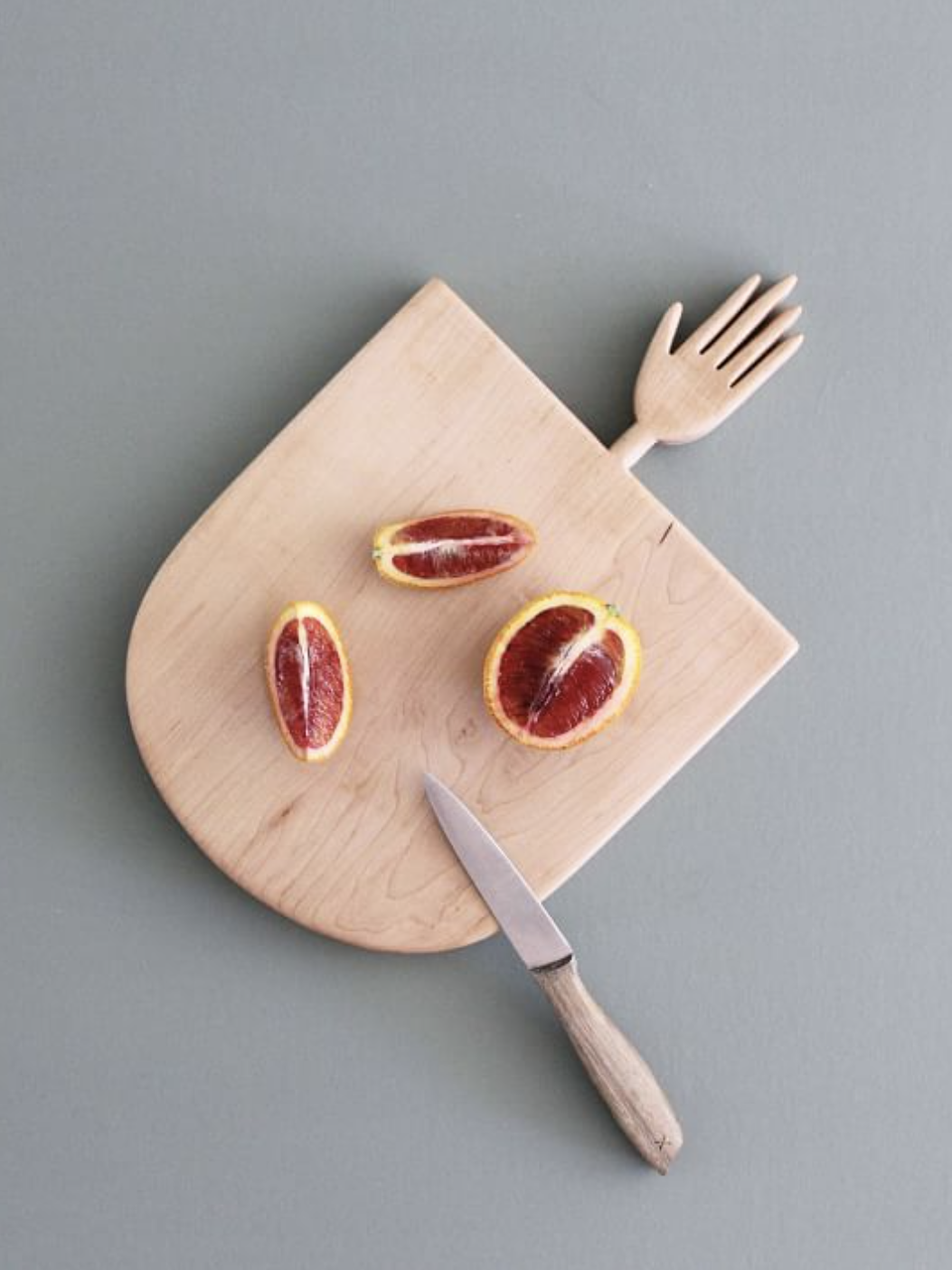 Sliced blood oranges on a wooden cutting board with a knife. Board has an integrated fork design.